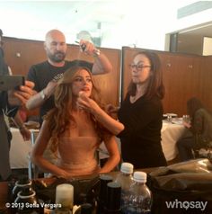 a woman is getting her hair cut by two men in front of a table with other people