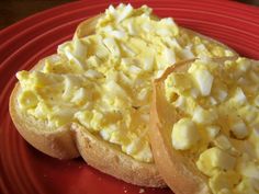 two pieces of bread with scrambled eggs on them sitting on a red plate next to another piece of toast