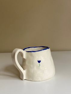 a white ceramic pitcher with blue handles on a table