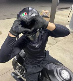 a man sitting on top of a motorcycle wearing black gloves and holding his hands to his face