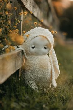 a stuffed animal sitting in the grass next to a wooden fence with flowers around it