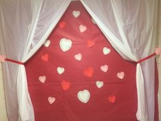 a red and white backdrop with hearts hanging from it's sides in front of a window