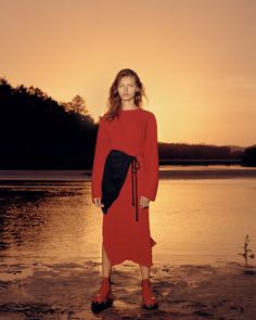 a woman in a red dress stands on the beach at sunset with her legs crossed