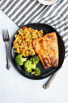 a black plate topped with meat, rice and broccoli next to a fork