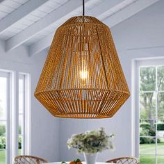 a wicker light hanging over a dining room table with chairs and vases on it