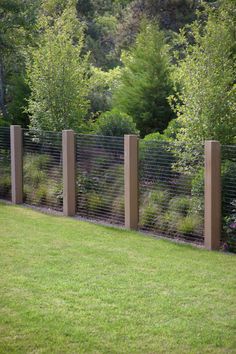 a fenced in area with green grass and bushes next to it is surrounded by tall wooden posts