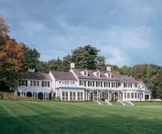 a large white house sitting in the middle of a lush green field next to trees