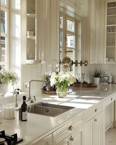 a white kitchen with lots of counter space and flowers in the window sill on the sink