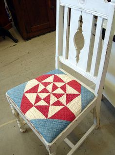 a white chair with a red and blue quilt on it's seat, sitting in a room