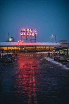 the public market sign is lit up in red and yellow lights at night, along with cars parked on the side of the road