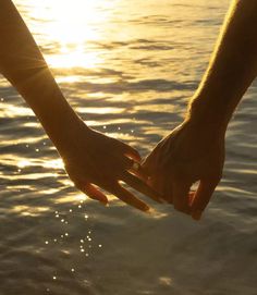 two people holding hands over water with the sun setting in the background and shining on them