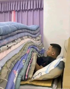 a man laying on top of a bed covered in blankets next to a pile of folded shirts