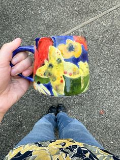 a person holding a coffee mug in their left hand while sitting on the ground next to them