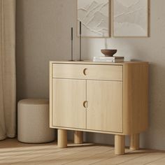 a wooden cabinet with two pictures on the wall above it and a stool next to it