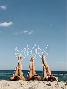 three women laying in the sand with their feet up on each other's heads