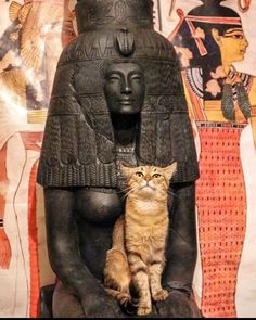 a cat sitting on top of a statue next to a wall with egyptian art behind it