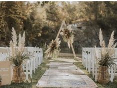 an outdoor ceremony set up with white chairs and flowers in vases on the aisle