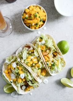 three tacos with mango salsa and limes on the side