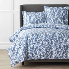 a blue and white comforter set on a bed with leaves in the air above it