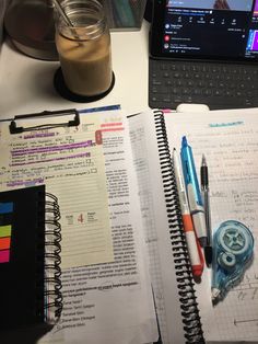 an open notebook sitting on top of a desk next to a laptop computer and a cup of coffee