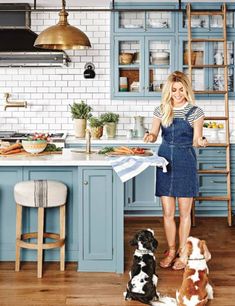 a woman standing in a kitchen next to two dogs