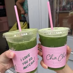 two people holding up cups with green smoothies in them