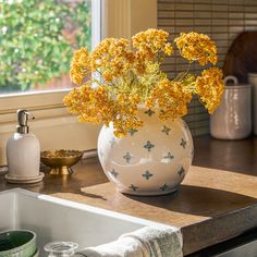 a white vase filled with yellow flowers sitting on top of a counter next to a sink