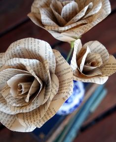 two paper roses sitting on top of each other in front of a book page vase