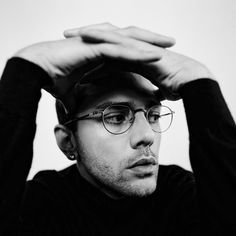 black and white photograph of a man with glasses holding his hands to his head while looking at the camera