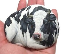 a hand holding a small black and white cow painted on it's face with horns