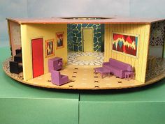 a doll house with furniture and paintings on the walls, sitting on a green surface