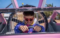 a man driving a pink car with his hands on the steering wheel and wearing sunglasses