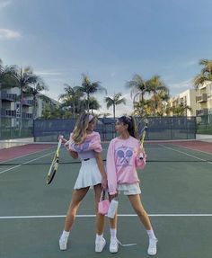 two young women standing on a tennis court holding racquets and talking to each other