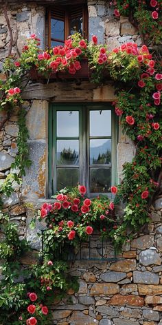 an old stone building with red flowers growing on the windowsill and green shutters