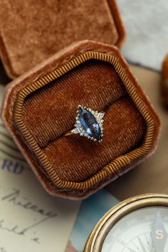 an engagement ring sits in a velvet box next to a pocket with a watch on it