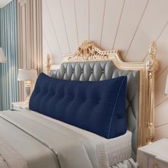 a bed with a blue pillow on top of it next to a night stand and lamp