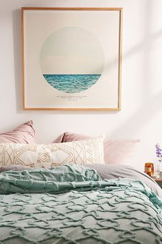 a bed with pillows and blankets on top of it next to a framed art piece