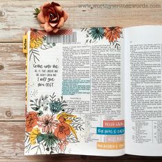 an open bible on a wooden table with a flower in the middle and words above it