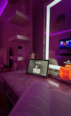 an open book sitting on top of a table in front of a tv screen and purple lighting