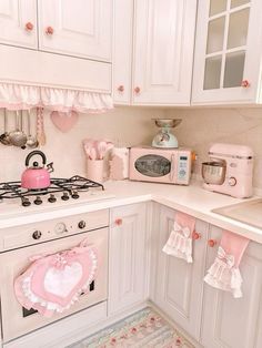 a kitchen with white cabinets and pink accessories on the stove top, along with an oven