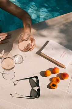 two people are sitting at a table with glasses and an open book by the pool