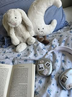 two stuffed animals sitting on top of a bed next to an open book and headphones