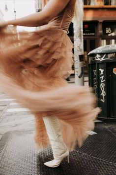 a woman in white boots is dancing on the street with her dress flowing over her