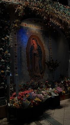 an altar with flowers and candles in front of the virgin mary statue at night time