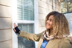 a woman is smiling and pointing to the side of a house with her hand on the door handle