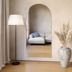 a living room with a white couch and a mirror on the wall next to a floor lamp