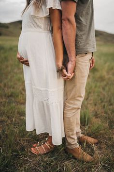 a man and woman holding hands while standing in the middle of a field with grass