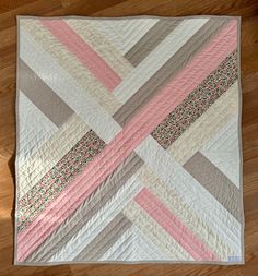 a pink, grey and white quilt is on the floor next to a wooden floor