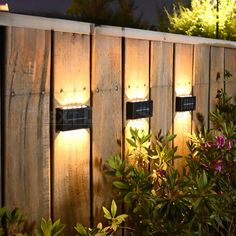 three lights are on the side of a wooden fence with plants in front of it