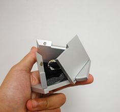 a hand holding an open metal box with a ring in it's center, on a white background